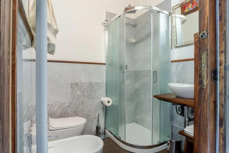 Bagno con doccia ad angolo e mensola in legno